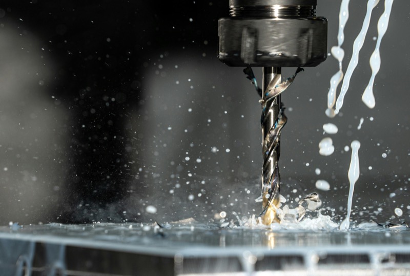 CNC drill bit in action with coolant spray during precision machining